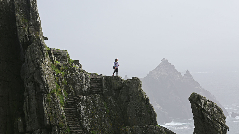 Un randonneur se tient au sommet de Skellig Michael, dans le comté de Kerry, contemplant les rochers déchiquetés sous un ciel brumeux.