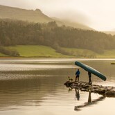 A person carries a canoe by Lough Gill at sunset, with forested hills and still waters in County Sligo.