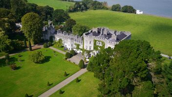 Aerial view of an Irish castle surrounded by lawns and trees under a clear blue sky.