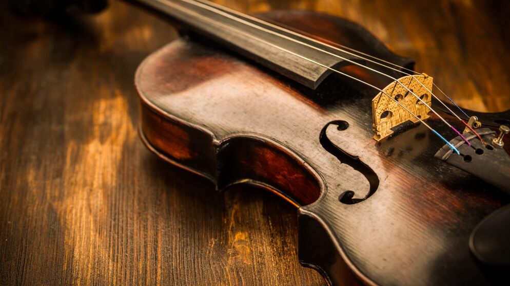 Primer plano de un violín irlandés desgastado sobre una mesa de madera, con su puente dorado y su cuerpo cálido iluminados suavemente para mostrar su fina artesanía.
