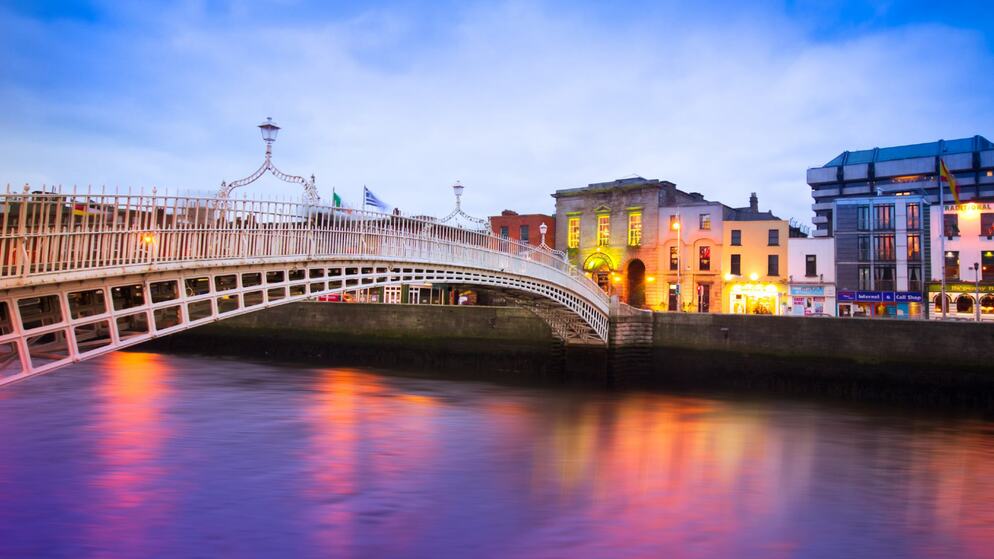Twilight view of Dublin’s Ha’penny Bridge lit in gold, city lights glowing behind.