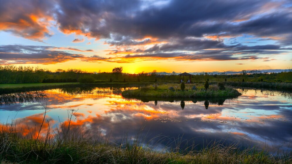 Puesta de sol sobre un lago tranquilo con nubes dramáticas y un mirador de madera en la orilla en Willowbrook Glamping, Roscommon.