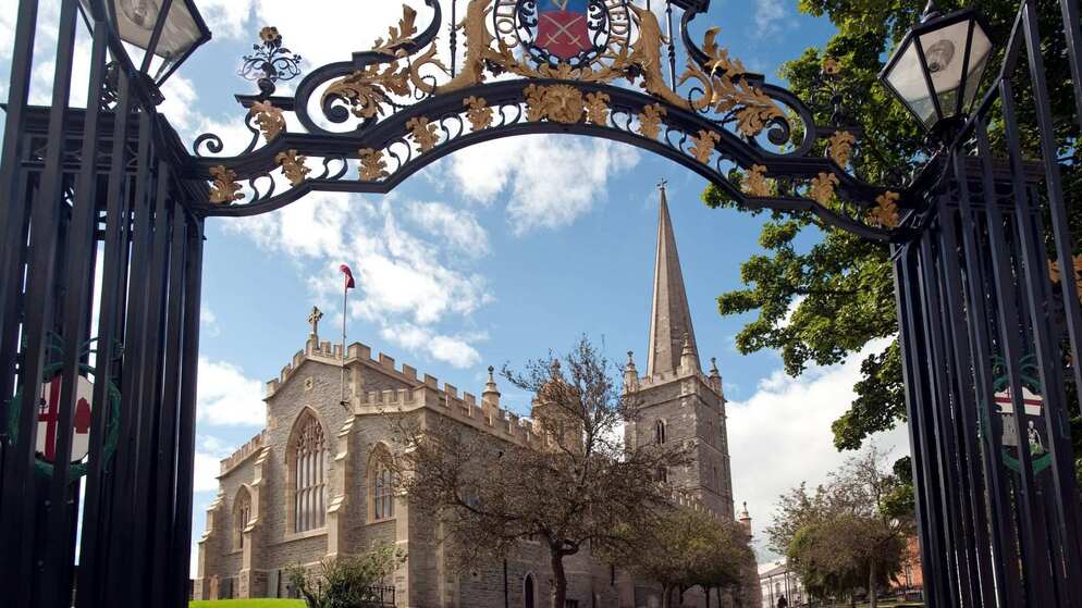 Dekoratives Schmiedeeisentor, das den Blick auf St Columb's Cathedral, Derry~Londonderry einrahmt, mit dem sich in den Himmel erhebenden Turm.