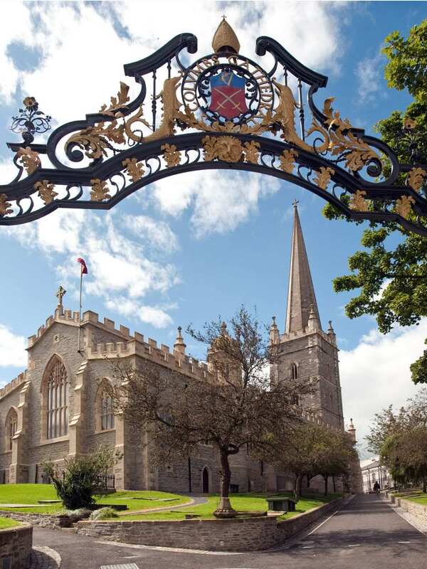 Decorative wrought-iron gate framing the view of St Columb's Cathedral, Derry~Londonderry, with spire rising into the sky.