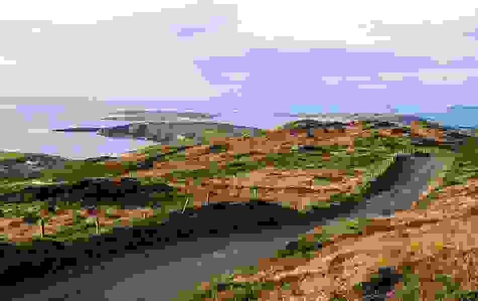 Küstenansicht von der Sky Road in Clifden, wo eine schmale Asphaltstraße sich durch zerklüftete Hügel in Richtung der Atlantikinseln schlängelt.