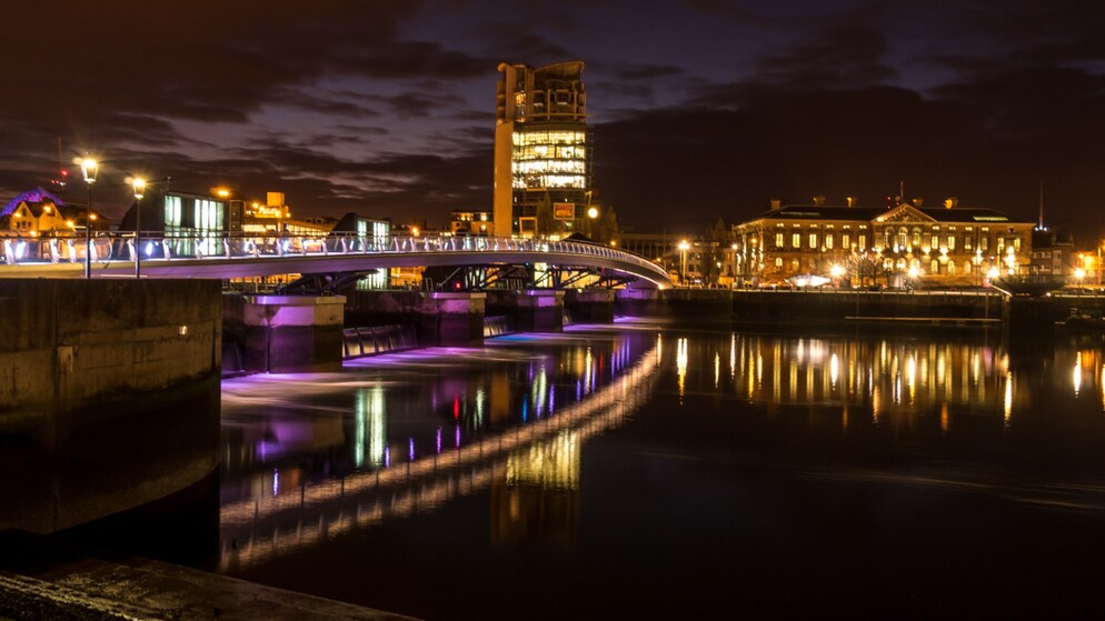 Ponte pedonale sul fiume Lagan illuminato con luci viola a Belfast di notte.