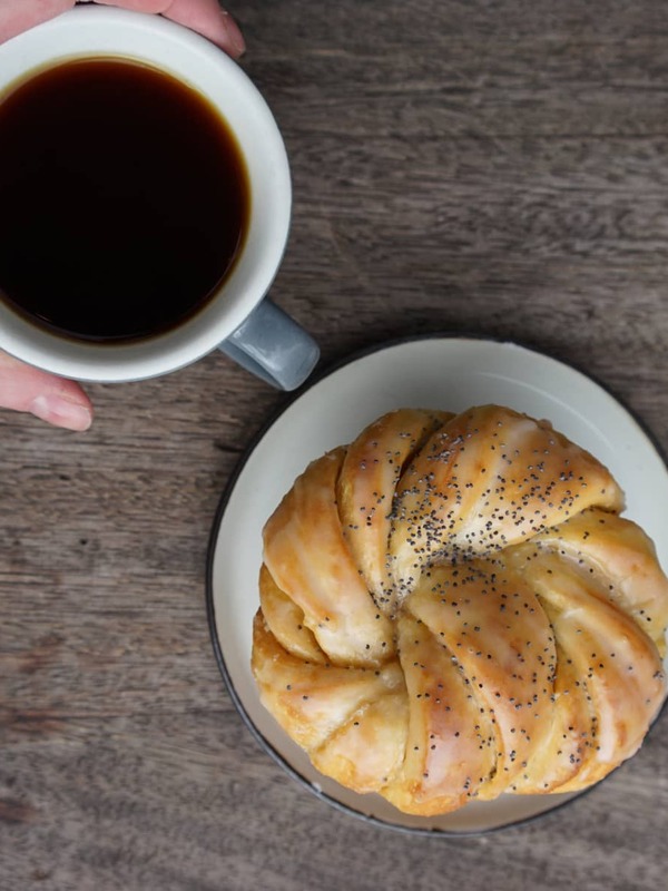 Hand holding a cup of black coffee beside a poppy seed pastry on a wooden table in Belfast café.