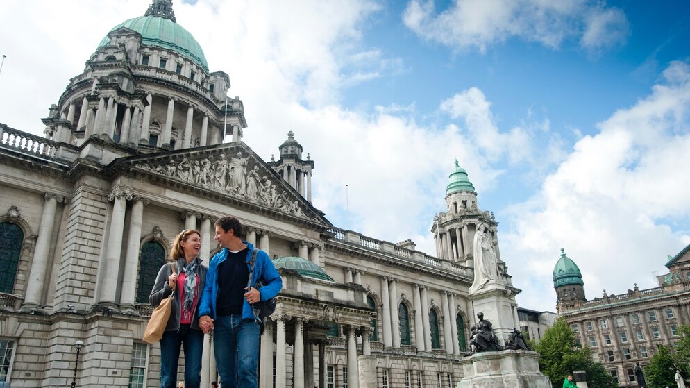 Couple outside Belfast City Hall, a landmark with green dome and ornate stone architecture.