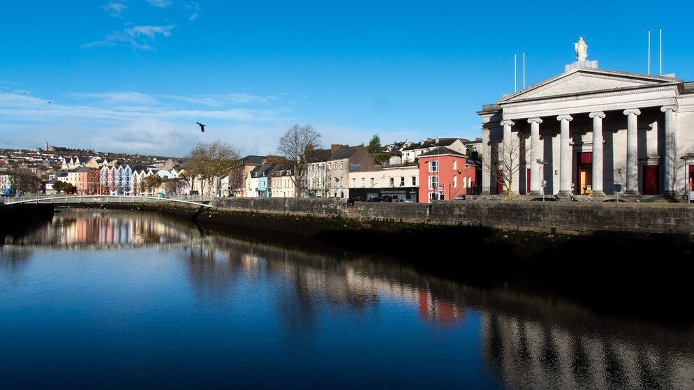 Colourful riverside buildings and a neoclassical courthouse reflected in the River Lee.