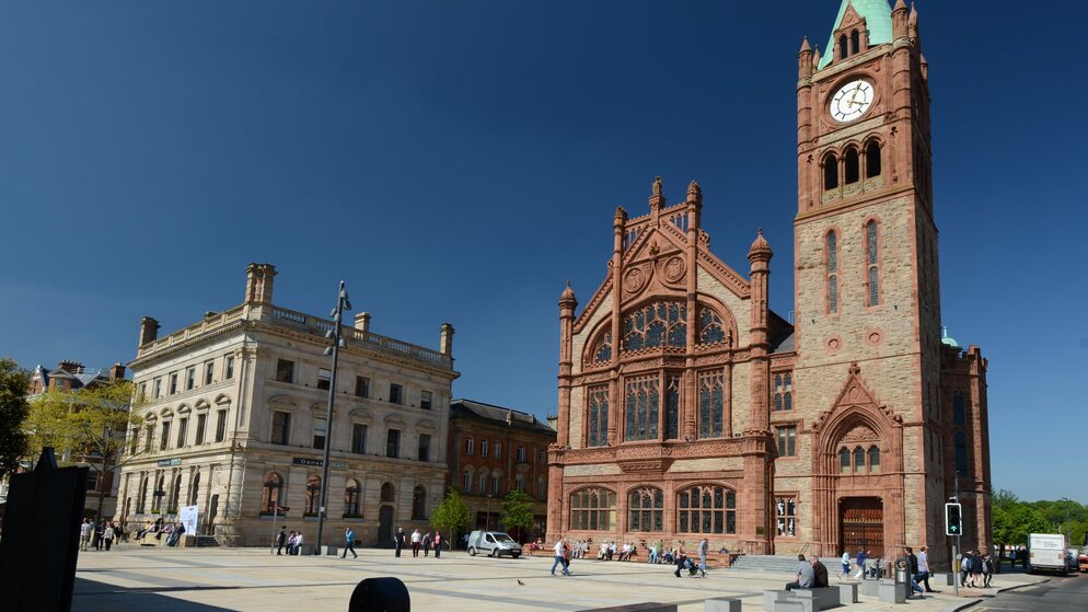 Derry~Londonderry’s Guildhall with red sandstone façade and clock tower rises against a blue sky, seen from Guildhall Square.