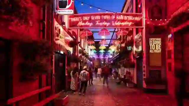 Ombrelli al neon e insegne luminose illuminano Commercial Court nel Cathedral Quarter di Belfast al tramonto.