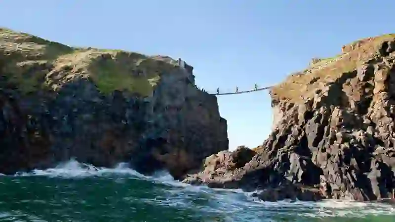 Le persone attraversano il ponte di corda di Carrick-a-Rede tra le scogliere rocciose sopra il mare nella contea di Antrim.