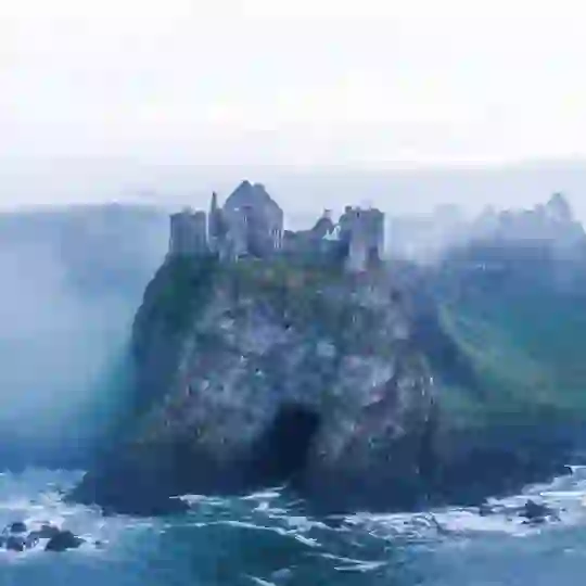 Le rovine del Dunluce Castle sopra una grotta sulla costa della contea di Antrim, circondate da nebbia e foschia.
