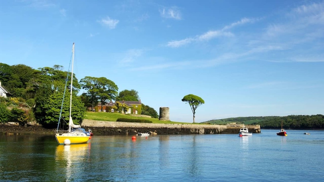 Boten aangemeerd op het rustige water van Strangford Lough, naast een door bomen omzoomde kustlijn in County Down.