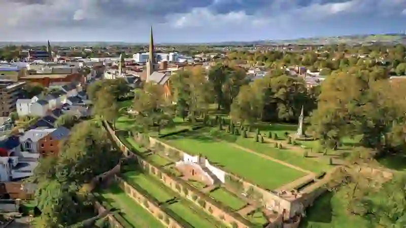 Blick über die Stadt Lisburn mit den Schlossgärten, historischen Kirchen und der umliegenden Landschaft unter eindrucksvollem Himmel.