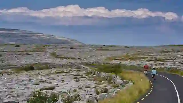 Des cyclistes roulent le long d'une route à travers le paysage calcaire du Burren, dans le comté de Clare, sous un ciel menaçant.