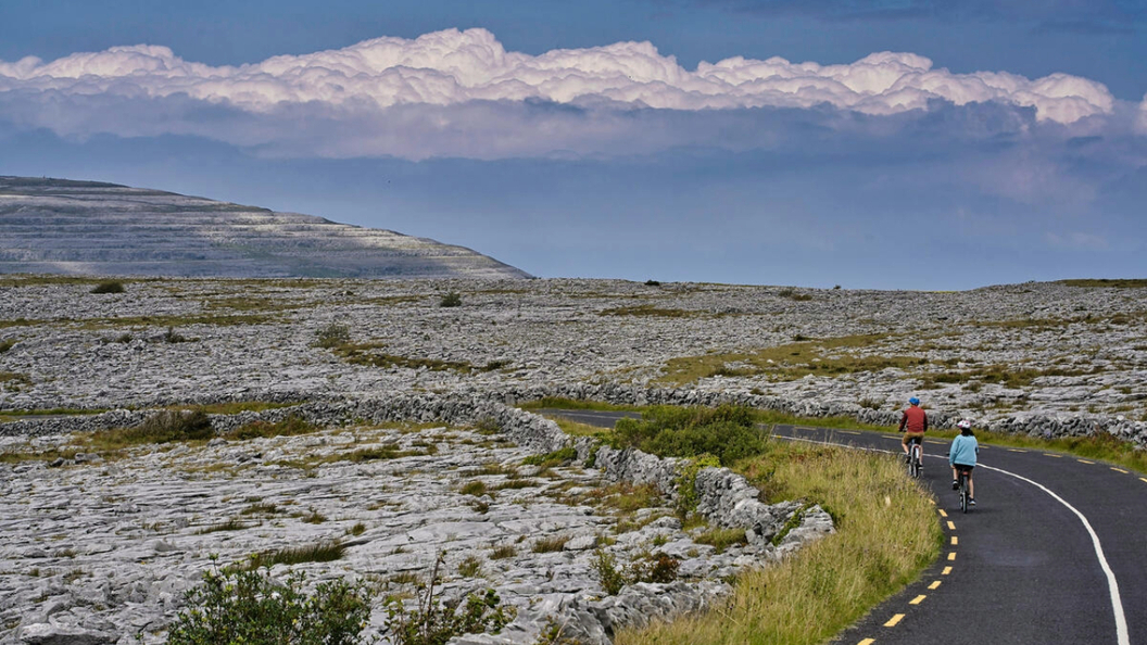 Des cyclistes roulent le long d'une route à travers le paysage calcaire du Burren, dans le comté de Clare, sous un ciel menaçant.