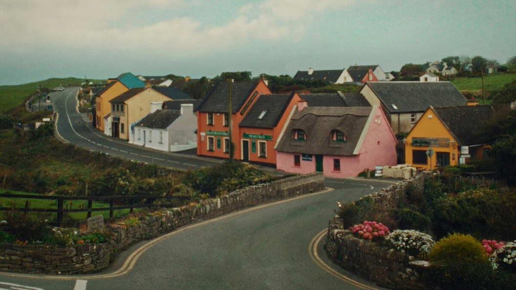 Des maisons et des boutiques colorées bordent une route sinueuse à travers le village de Doolin, dans le comté de Clare, sous un ciel nuageux.