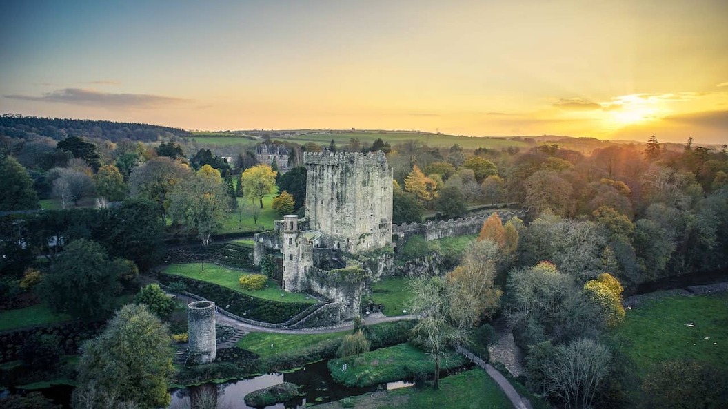 Blarney Castle and gardens, County Cork, with historic tower, river and lush woodland at sunset.