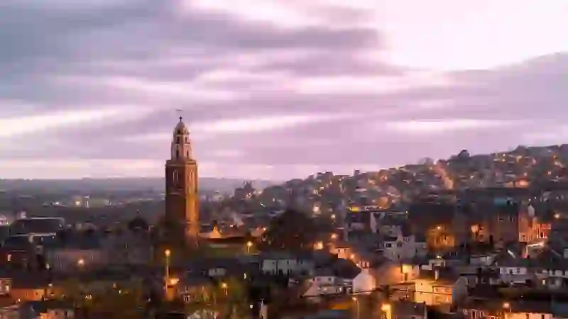 Cork City skyline at dusk with St Anne’s Church tower and glowing city lights under evening sky.
