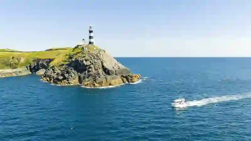 Old Head of Kinsale lighthouse, County Cork, on rugged cliffs above the Atlantic Ocean with passing boat.