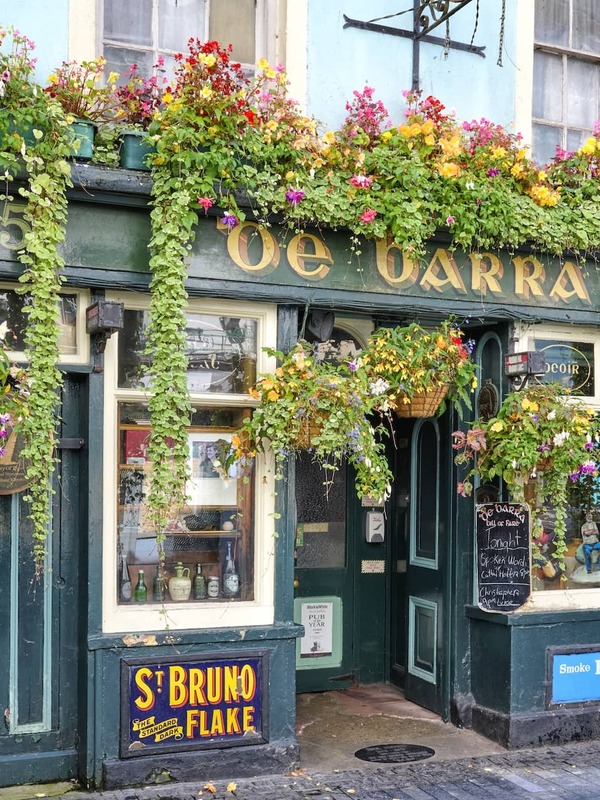 Buitenkant van De Barra's pub in Clonakilty, West Cork, met kleurrijke bloemen en een traditionele Ierse gevel.