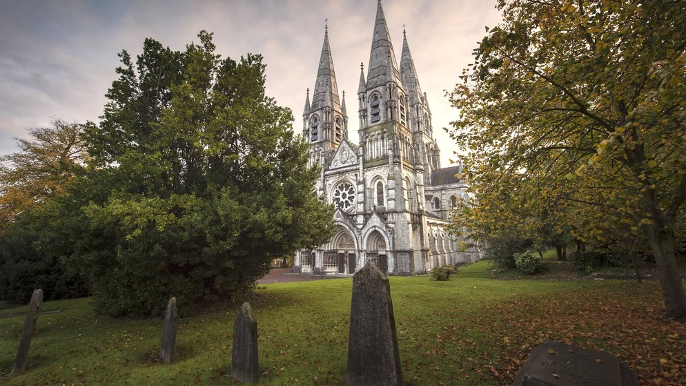 St Fin Barre’s Cathedral in Cork City, gothic spires rising above autumn trees and historic graveyard.