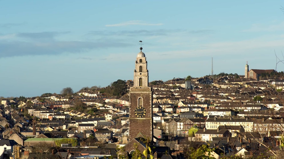 Shandon Bells tower and Cork city skyline, with historic clock tower above rooftops in warm evening light.