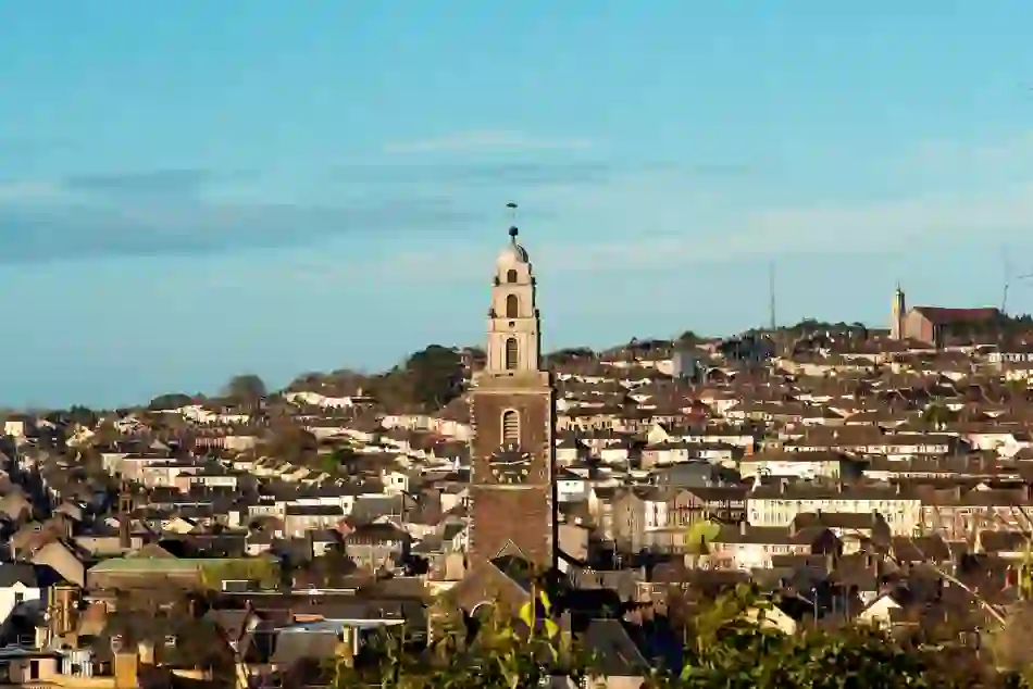 Shandon Bells tower and Cork city skyline, with historic clock tower above rooftops in warm evening light.