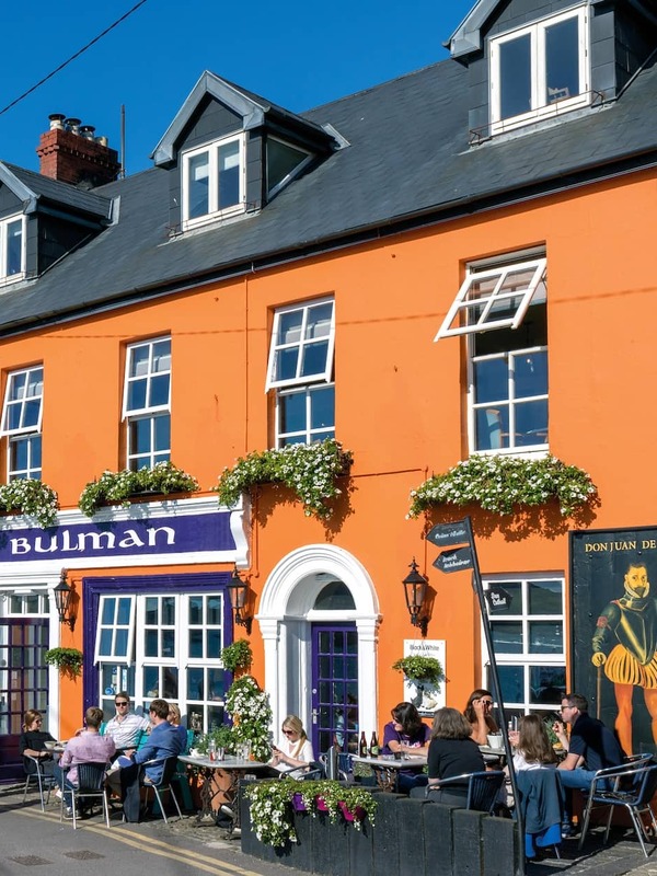 Buitenkant van de Bulman pub in Kinsale, county Cork, met een feloranje gevel en terras aan een zonnige straat.