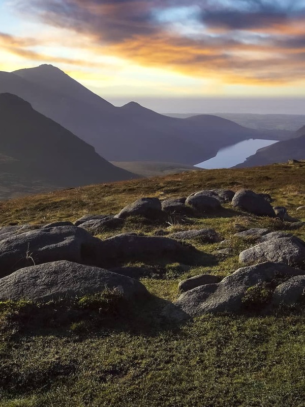 Zonsopgang over de Mourne Mountains in county Down, met ruige bergtoppen, een vallei naast een meer en een tent met uitzicht op het landschap.