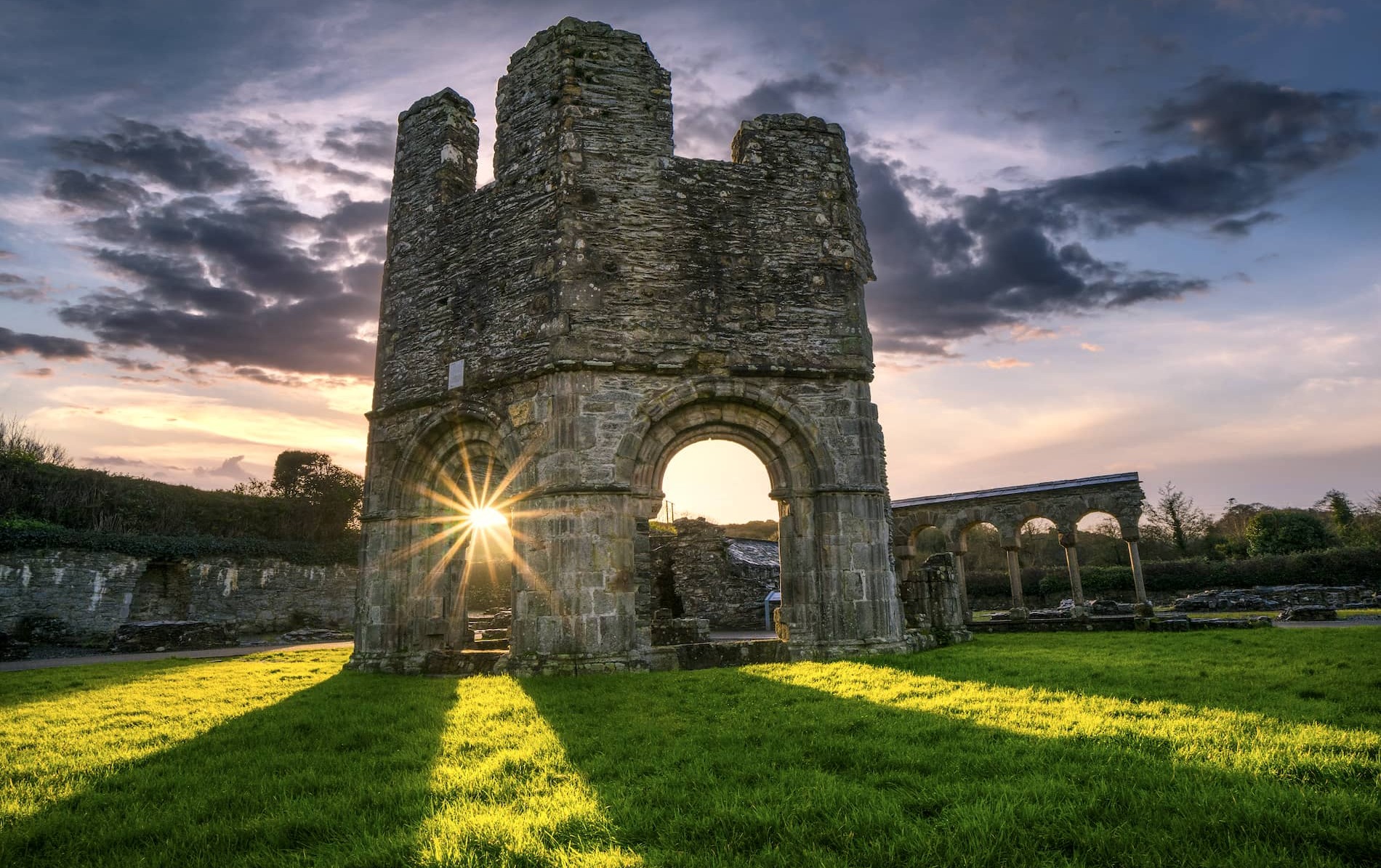 Mellifont Abbey ruins in County Louth at sunset with ancient stone arches, dramatic skies and long shadows across the grass.