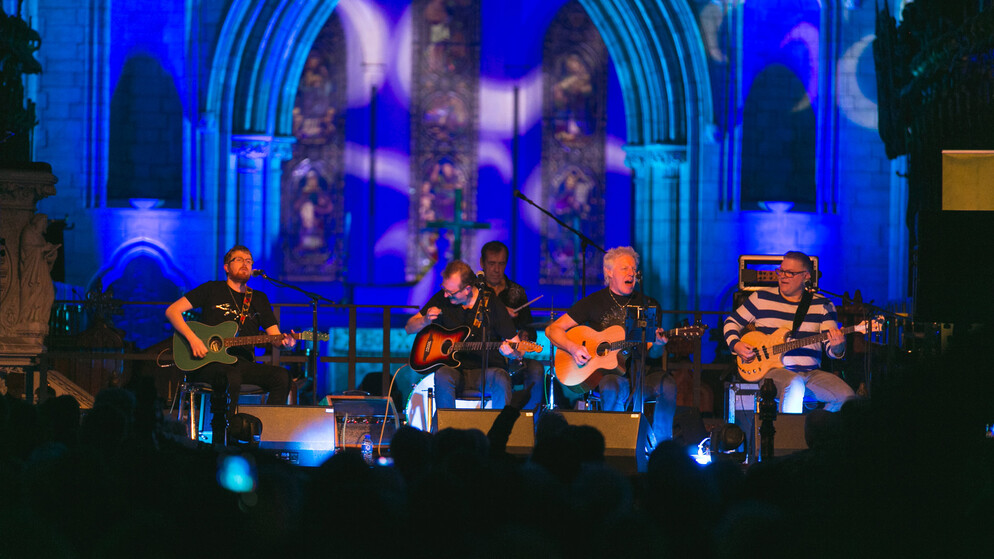 Eine Blaskapelle in farbenfrohen Outfits sind während einer Live-Aufführung in Dublin zu sehen. In der Szene ist zu sehen, wie sie mit viel Energie und Bewegung auftreten.