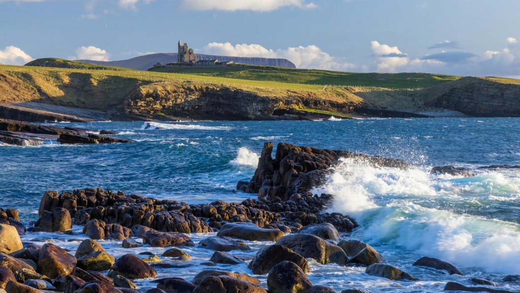Las olas rompen contra la costa rocosa de Mullaghmore, con el castillo de Classiebawn con vistas a la costa del condado de Sligo.