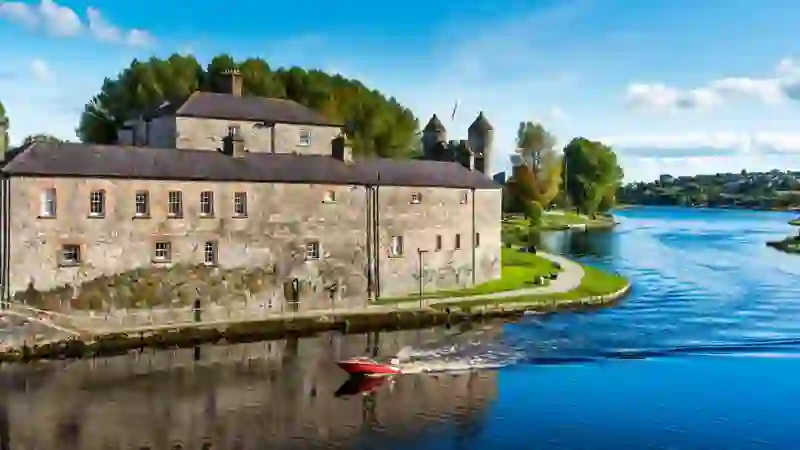 Enniskillen Castle beside the River Erne as a red motorboat passes on a bright sunny day.