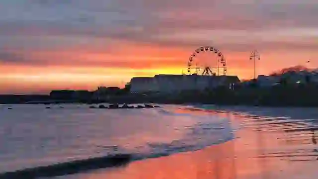 Promenade et plage de Salthill à Galway au soleil couchant, avec grande roue se reflétant sur le rivage.