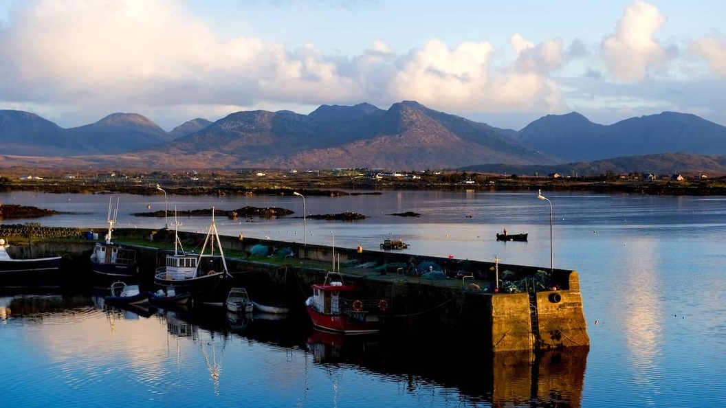 Le Port de Roundstone dans le Connemara avec ses bateaux de pêche sur des eaux calmes et des montagnes se dressant au loin, dans le comté de Galway.