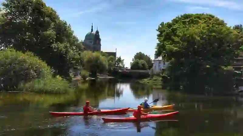 Kayakistes sur la rivière Corrib à Galway avec cathédrale, pont et arbres se reflétant dans une eau calme.