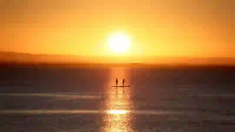 Silhouettes de paddleboarders dans la baie de Galway au soleil couchant, et reflets dorés sur la mer.