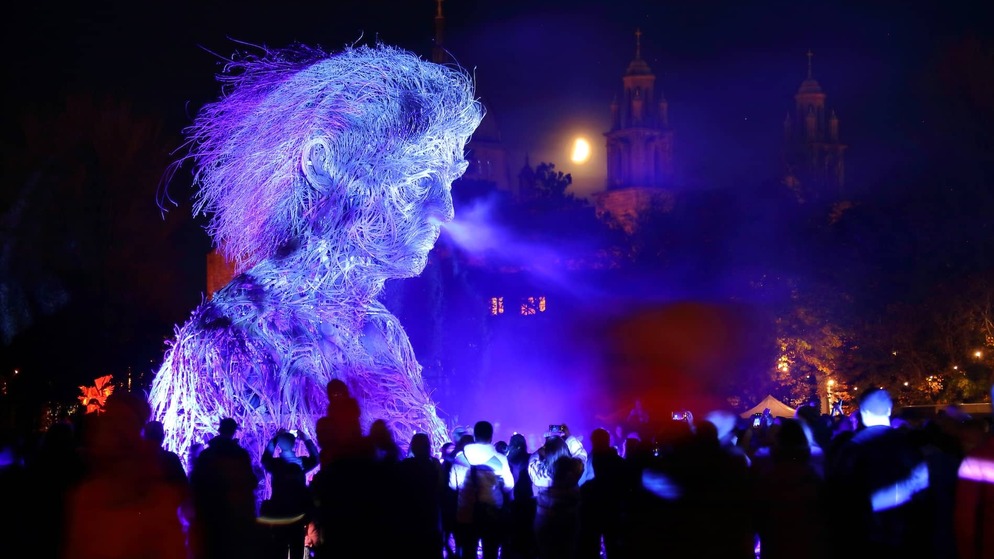 Crowds gathered around a glowing Macnas parade figure during Galway International Arts Festival at night.