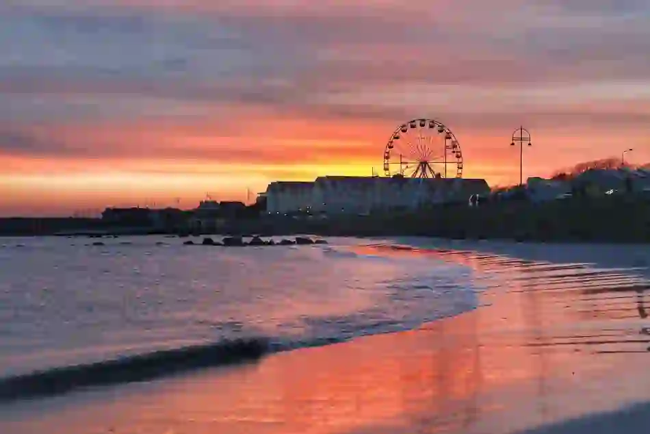 Ferris wheel beside Salthill beach at sunset with colourful skies reflected on the shoreline in Galway.