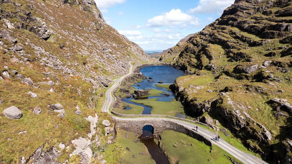 Aerial view of the Gap of Dunloe, with a winding road, stone bridge and mountain lake in County Kerry, Ireland.