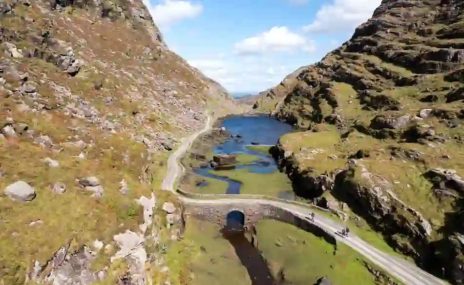 Aerial view of the Gap of Dunloe, with a winding road, stone bridge and mountain lake in County Kerry, Ireland.