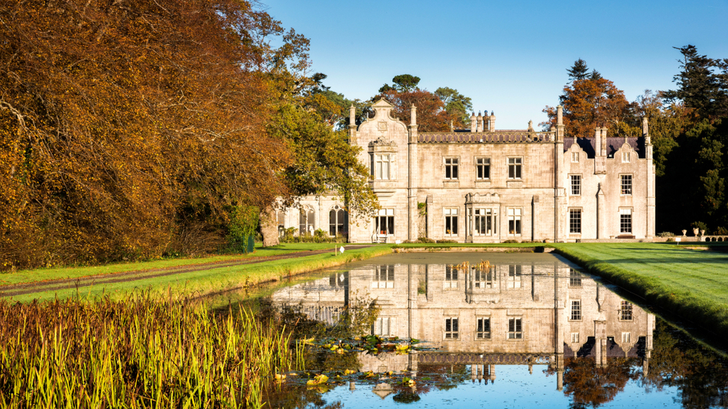 Kilruddery House reflected in a still pond, framed by autumn trees and manicured lawns in Bray, County Wicklow.