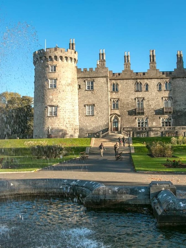 Kilkenny Castle reflected in a fountain, with manicured gardens and historic stone towers in Kilkenny city.