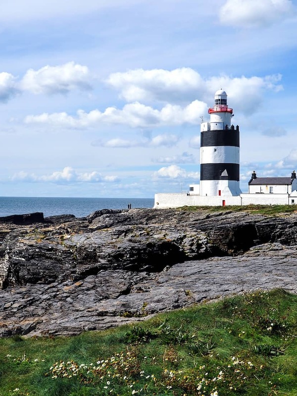Hook Head Lighthouse in County Wexford, striped tower overlooking rocky coast and calm blue sea.