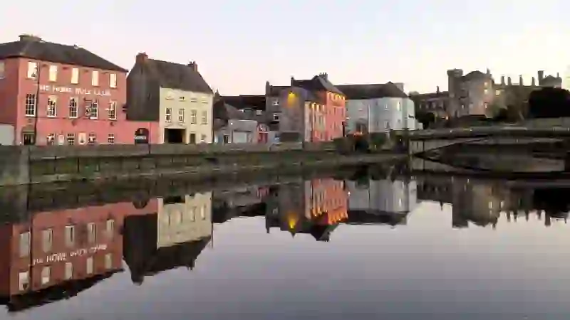 Ville de Kilkenny au crépuscule avec maisons au bord de l'eau, pont et château se reflétant dans la rivière Nore.