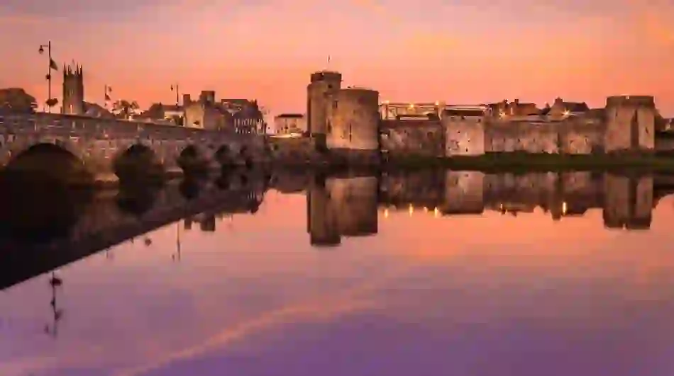 King John’s Castle and Thomond Bridge reflected in the River Shannon at sunset in Limerick city.