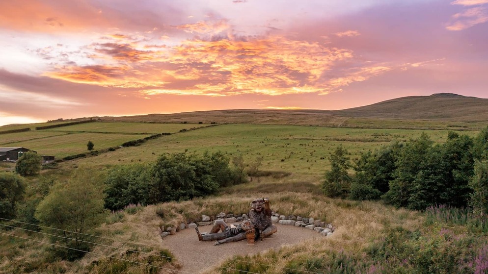 Wooden sculpture of giants in County Tyrone's Sperrin Mountains overlooking rolling countryside at sunset.