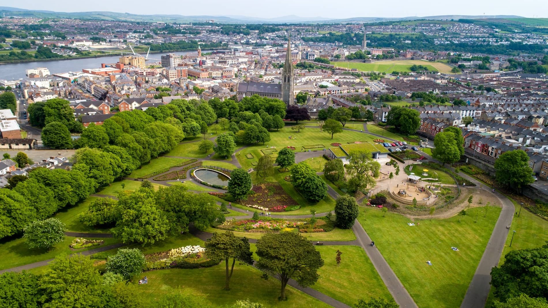 Aerial view of Brooke Park with gardens and Derry~Londonderry city skyline beyond.